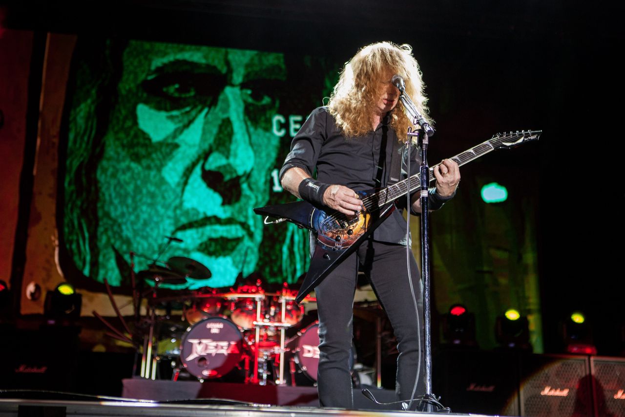 Dave Mustaine von Megadeth mit Gitarre am Mikrofon, hinter ihm eine grüne Porträt-Leinwand