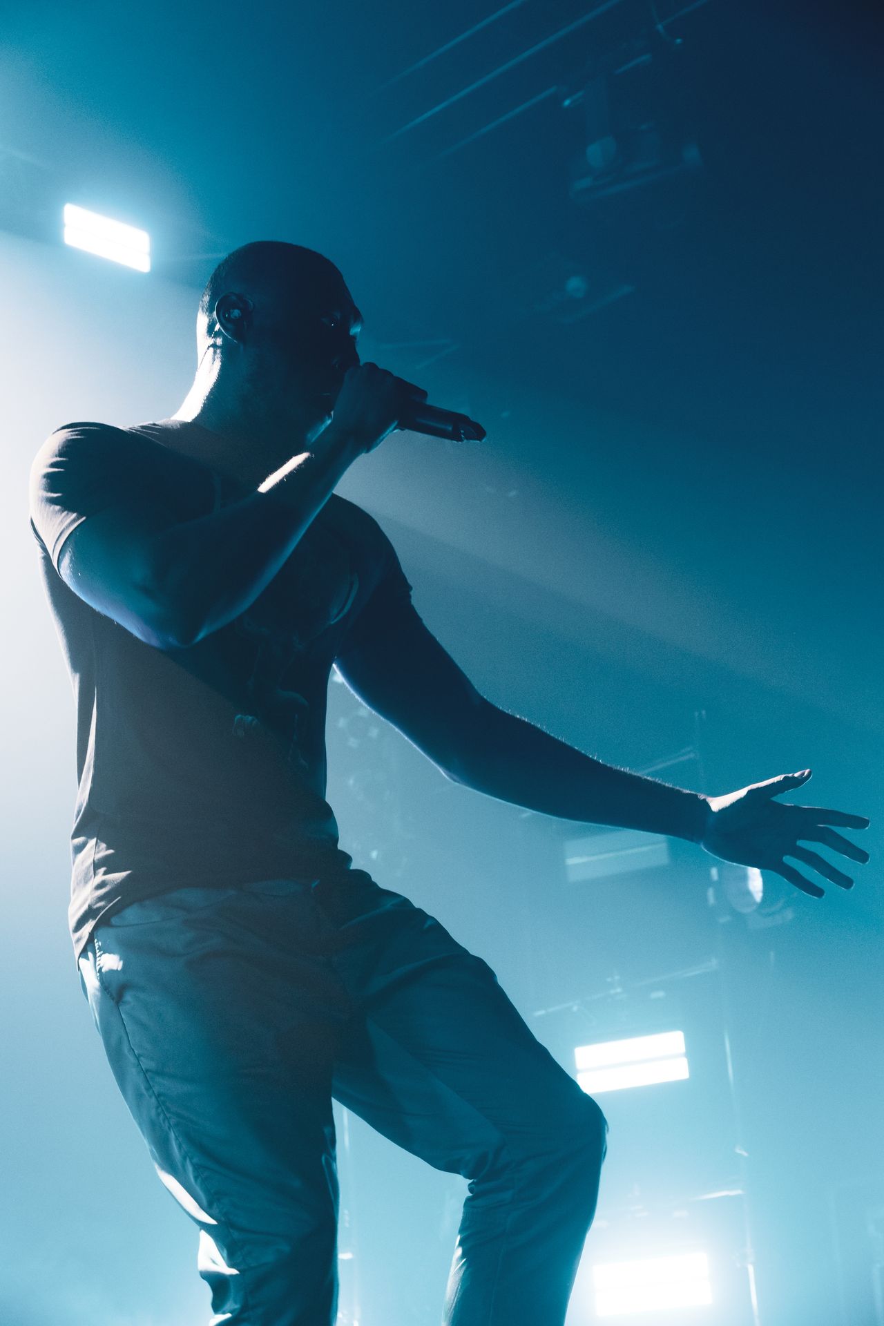 Stormzy im türkisfarbenen Gegenlicht, Mikrofon am Mund, Arm ausgestreckt