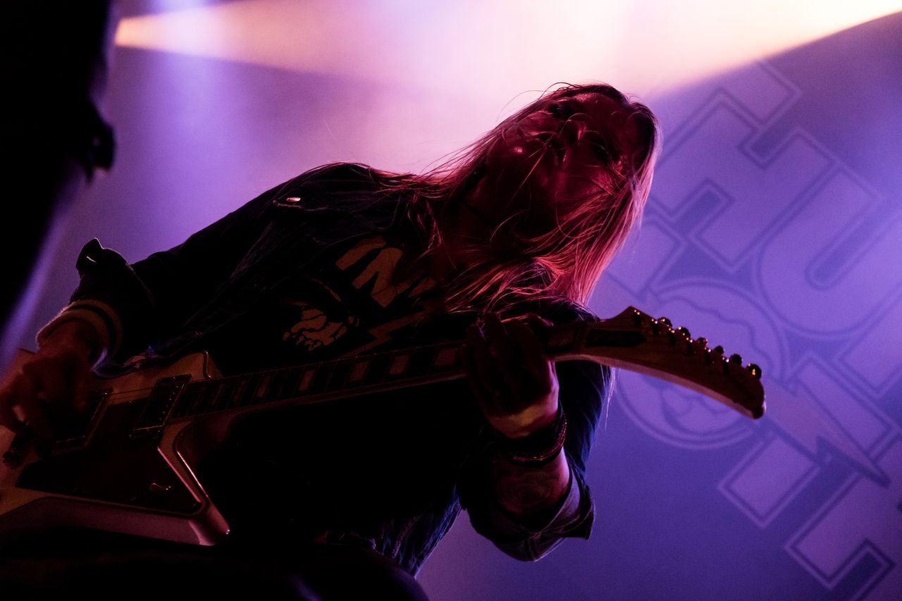 Thundermother-Gitarristin beugt sich mit wehenden Haaren über die Gitarre, Silhouette vor violettem Licht