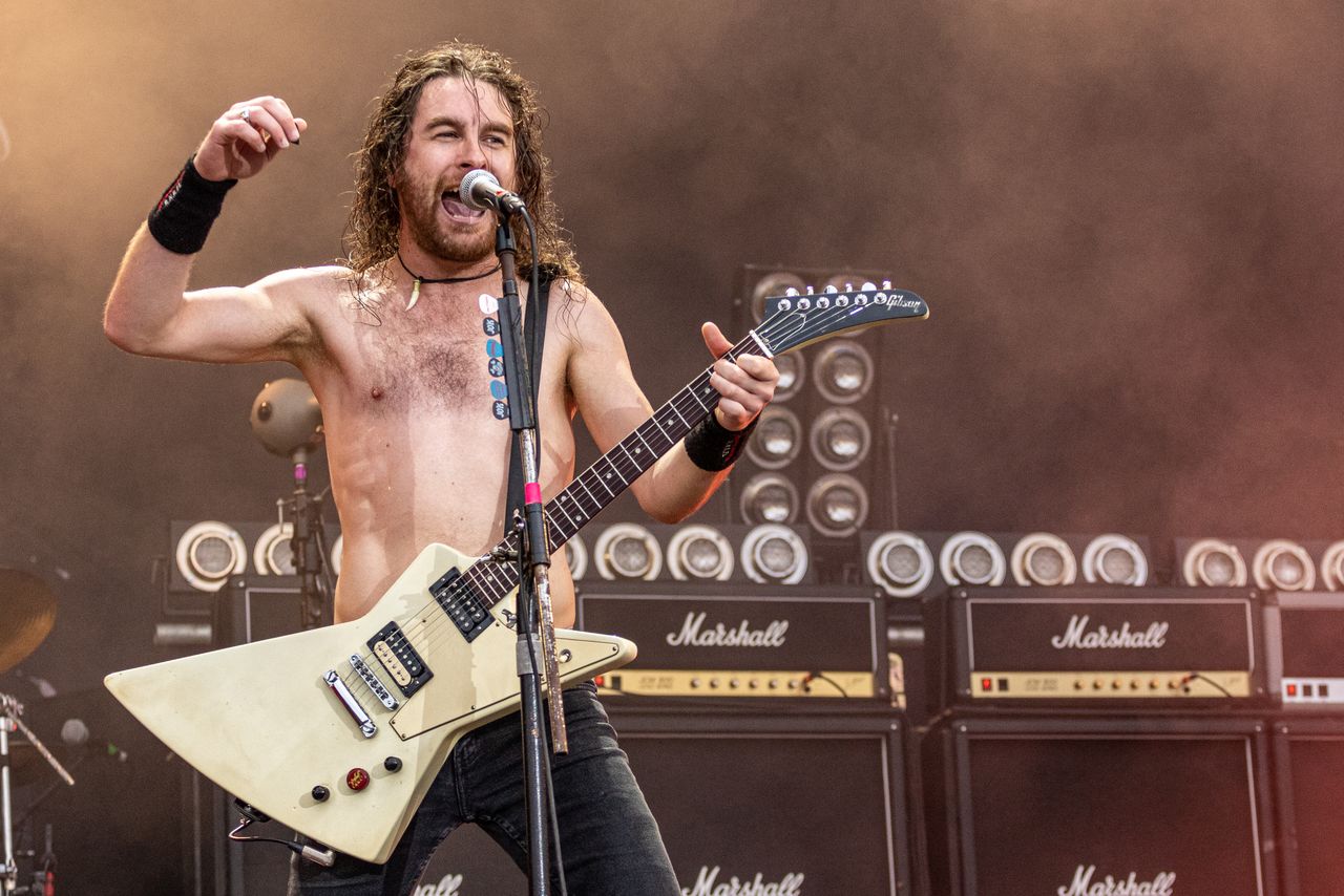 Airbourne-Sänger mit nacktem Oberkörper und weißer Explorer-Gitarre vor einer Wand aus Marshall-Verstärkern