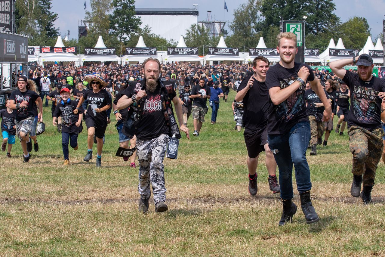 Metal-Fans rennen bei der Geländeöffnung lachend über die Wiese des Wacken Open Air