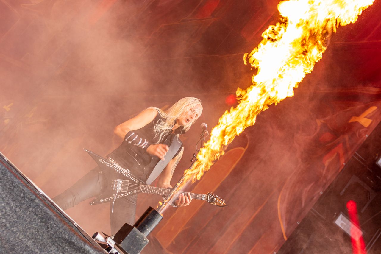 HammerFall-Gitarrist auf der Wacken-Bühne, neben ihm schießt eine meterhohe Flammensäule diagonal durch den Rauch