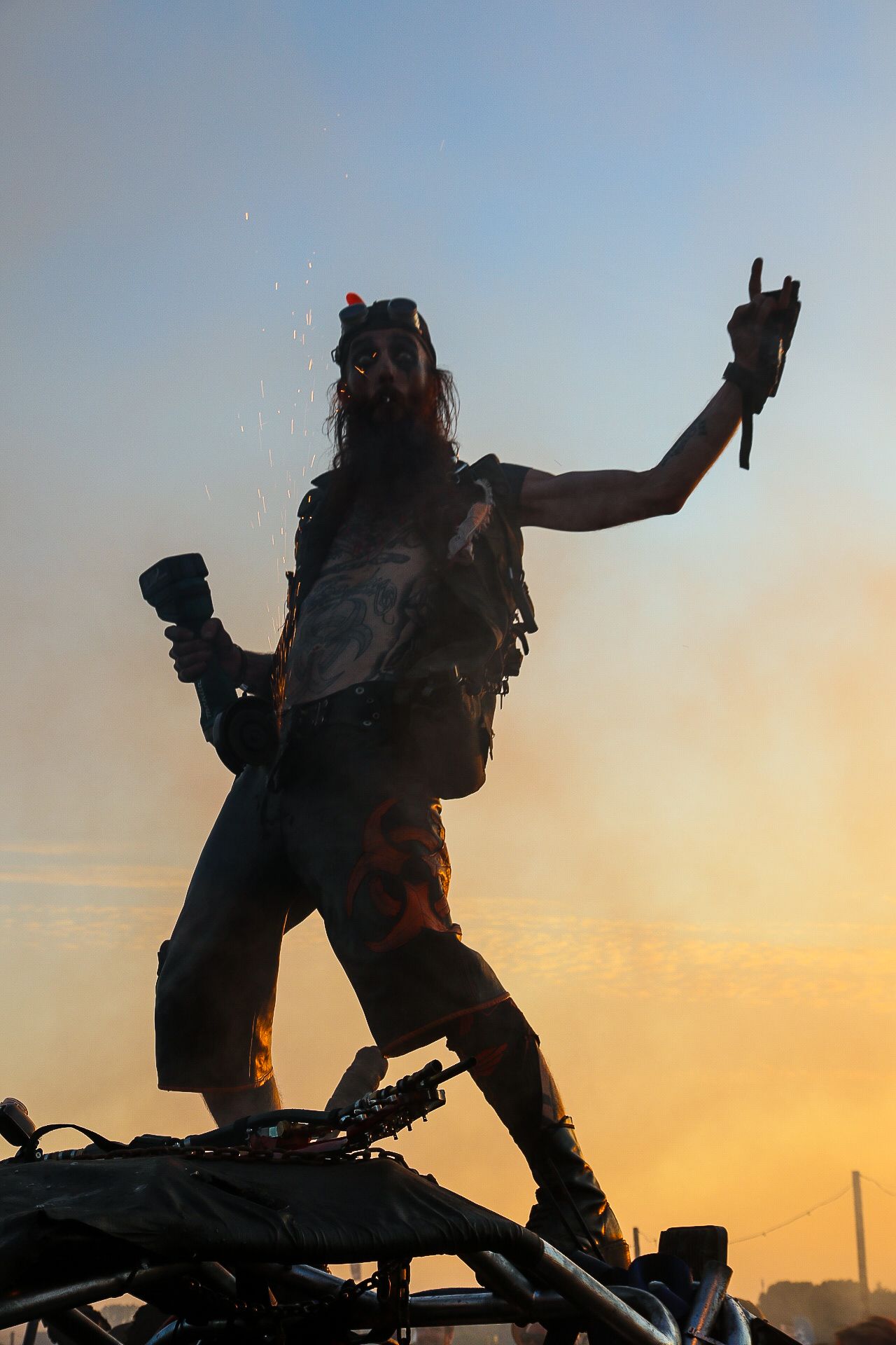 Kostümierter Festivalbesucher als Silhouette auf einem Fahrzeugdach vor orangefarbenem Abendhimmel
