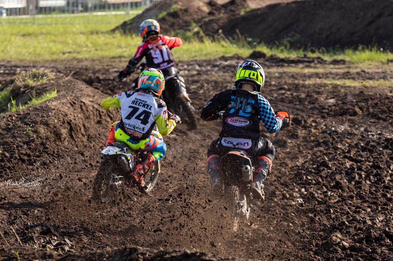 Drei junge Motocross-Fahrer in bunter Montur kämpfen sich durch die Schlammkurve